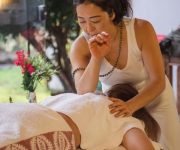 Terapeuta aplicando massagem com o cotovelo de forma sutil nas costa de uma mulher deitada com paisagem natural ao fundo.