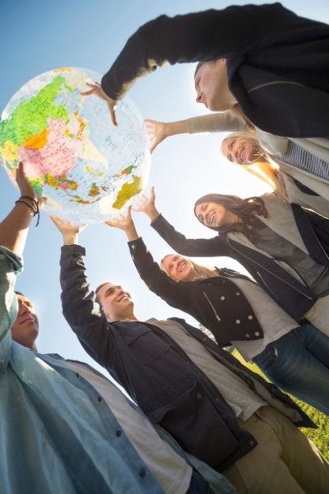 Seis pessoas seguram uma bola com o desenho de um mapa, levantando-a para o alto.